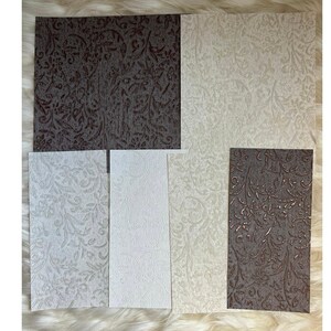May include: A collection of five rectangular sheets featuring an embossed floral and vine pattern. The set includes two dark brown sheets, one cream sheet, one light gray sheet, and one white sheet, all displaying a consistent textured surface.