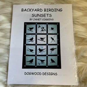 May include: A white instructional booklet titled Backyard Birding Sunsets by Janet Coggins from Dogwood Designs. The cover features a grid of twelve squares, each displaying a black silhouette of a bird perched on a branch against a blue background.