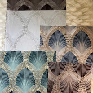 May include: A collection of five square wallpaper samples featuring a repeating fan-shaped geometric pattern. The color variations include dark brown, light gray, navy blue with gold accents, teal with gold accents, and a metallic bronze finish.