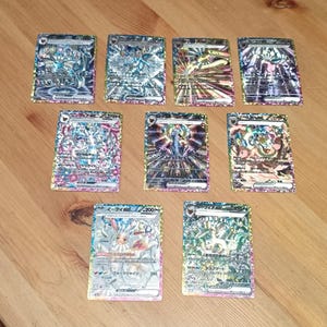 May include: Eight rectangular trading cards featuring colorful Japanese anime-style character illustrations with holographic foil details. Each card displays various stats, text, and symbols printed in Japanese, arranged in three rows on a surface.
