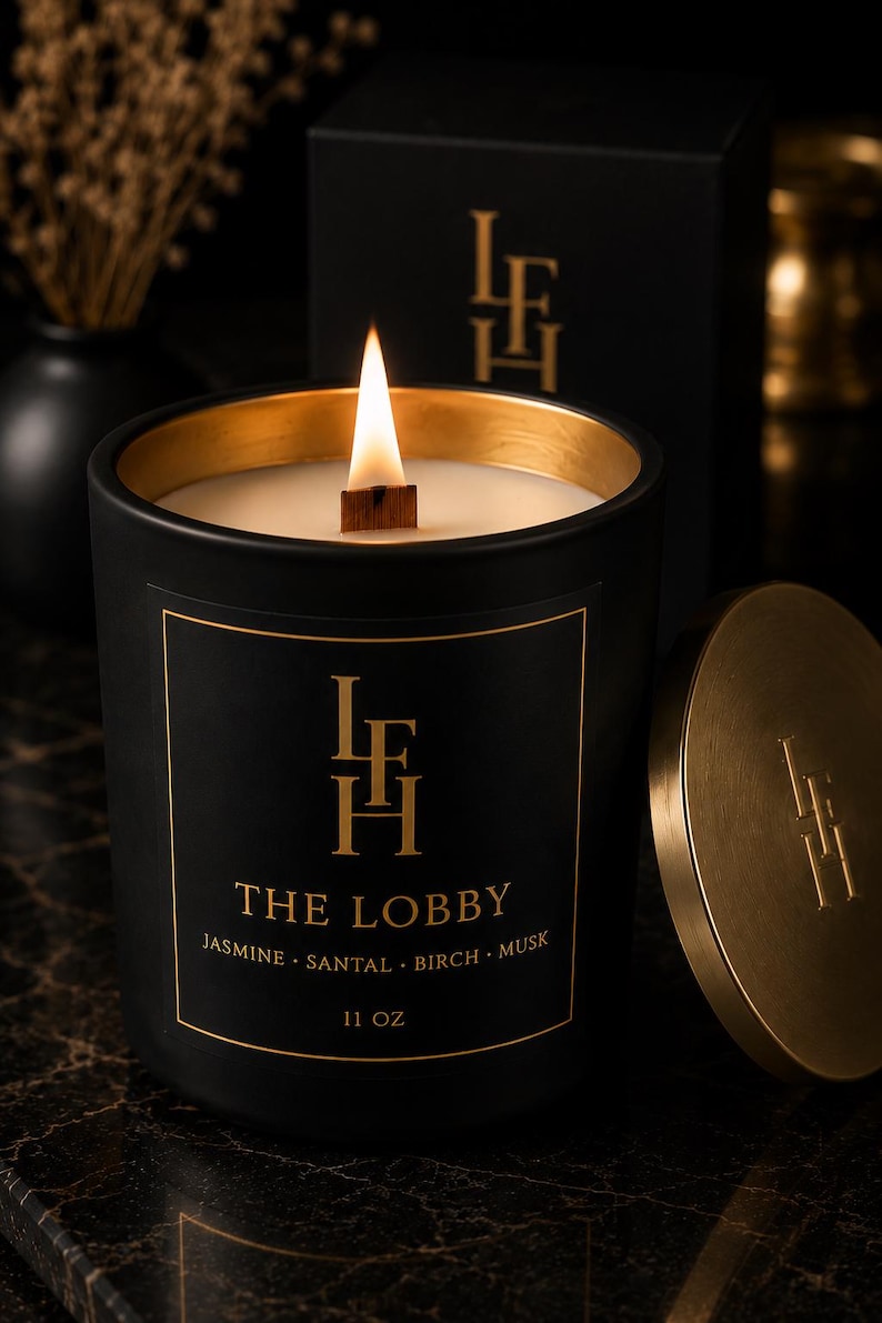 K&ouml;nnte beinhalten: Schwarze Kerze mit goldenem Rand und Deckel, beschriftet mit "THE LOBBY" und Duftnoten. Die Kerze hat einen Holzdocht und befindet sich in einer schwarzen Box. Die Kerze ist 312 Gramm.