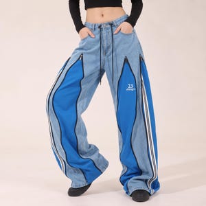May include: Light blue denim jeans featuring wide legs with contrasting bright blue fabric panels. The pants include black zippered accents along the seams, white side stripes, and the text 23 zhengru printed in white on the left leg.
