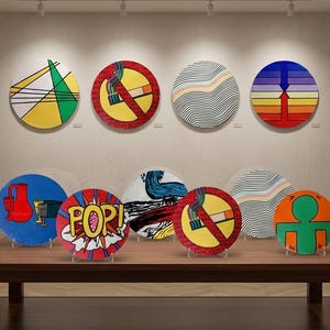 May include: A collection of colorful, round decorative art pieces displayed on a wooden table. The art features various designs, including geometric shapes, pop art, and a no-smoking symbol. The pieces are mounted on clear stands.