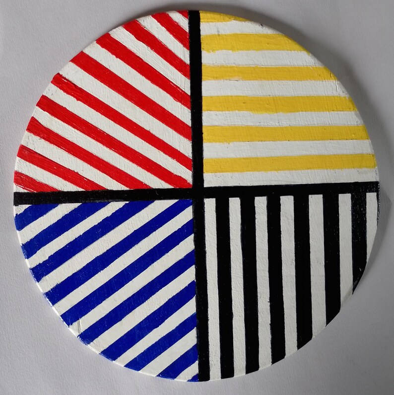 May include: A round, painted wooden art piece with a segmented design. The design is divided into four quadrants, each with a different pattern: red and white diagonal stripes, yellow and white horizontal stripes, blue and white diagonal stripes, and black and white vertical stripes.