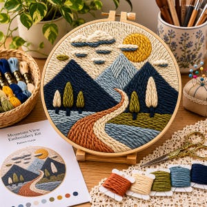 Op de afbeelding: Een ronde borduurring met een textuurrijk garenlandschap van donkerblauwe bergen, een lichtblauwe piek, een gele zon en een kronkelend oranje pad door groene velden, inclusief een patroongids en diverse kleuren borduurgaren.
