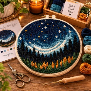 Könnte beinhalten: Ein besticktes Nachtszenen-Motiv in einem Holzrahmen. Das Kunstwerk zeigt eine Waldsilhouette unter einem Sternenhimmel in Blau-, Weiß- und Gelbtönen. Das Set enthält Stickgarn, eine Nadel und eine Schere. Auf der Karte steht "Stitch Create Relax".