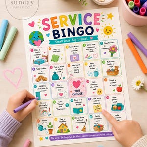 May include: A colourful "Service Bingo" game board with illustrations of kind acts in boxes. The board has text including "Small Acts. Big Impact." and "Be kind. Be helpful." A child's hand is drawing on the board with a purple marker.