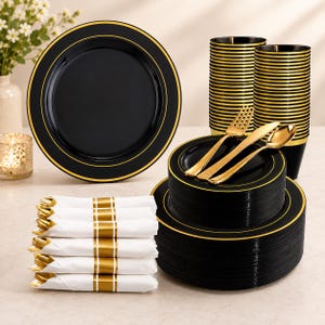 Puede incluir: Un juego de vajilla de plástico negro con bordes dorados, que incluye platos grandes y pequeños, vasos, tenedores, cuchillos y cucharas de plástico de color dorado, junto con servilletas de papel blanco envueltas con bandas doradas.