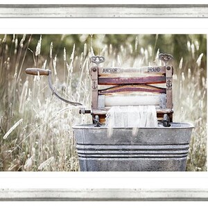 May include: An antique wooden washing machine with the words "Anchor Brand" printed on it, sitting in a metal tub in a field of tall grass.