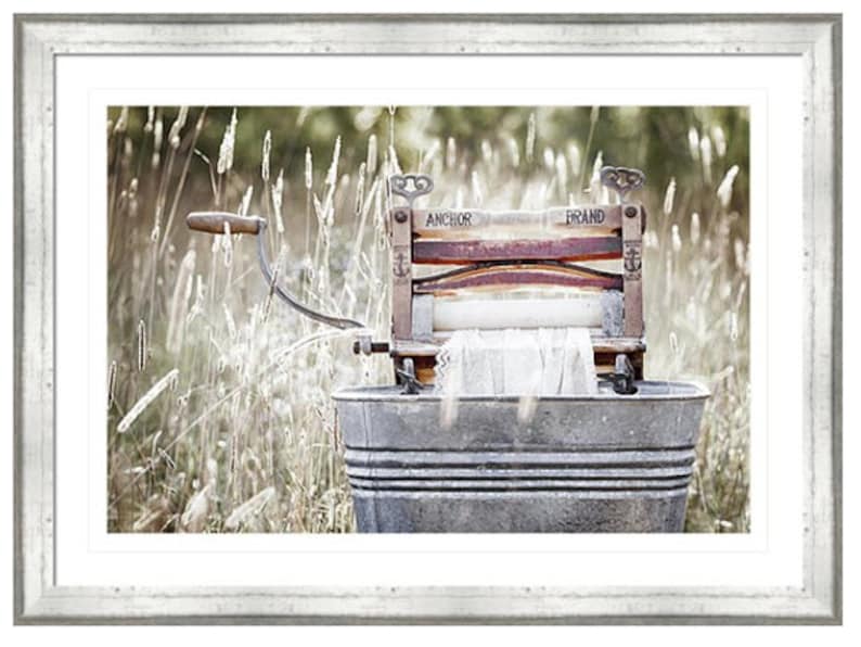 May include: An antique wooden washing machine with the words "Anchor Brand" printed on it, sitting in a metal tub in a field of tall grass.