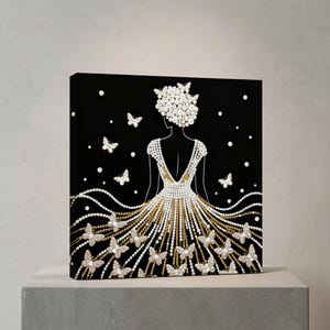May include: Black canvas art featuring a woman in a gown adorned with pearls and gold accents. White pearl butterflies and scattered pearls decorate the black background. The woman's hair is styled with pearls.
