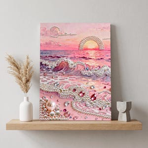 May include: A rectangular wall art piece depicting a pink sunset over an ocean scene. The artwork is embellished with white pearls and clear, pink, and iridescent rhinestones arranged to highlight the waves, the sun, and the clouds in the sky.