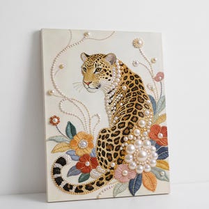 May include: A decorative canvas print featuring a leopard with pearl embellishments and floral embroidery. The leopard has a spotted coat and is adorned with pearls around its neck. Colorful embroidered flowers and leaves surround the leopard.