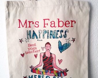 May include: A white canvas tote bag with a colorful design featuring a woman in a yoga pose. The text on the bag reads "Mrs Faber Happiness Best yoga teacher! Here & Now".