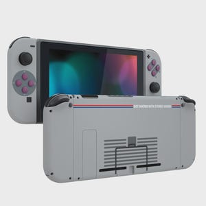 May include: A light gray handheld gaming console featuring a screen, detachable controllers with purple buttons, and a rear casing printed with the text DOT MATRIX WITH STEREO SOUND, accented by a thin horizontal blue and red stripe across the back.