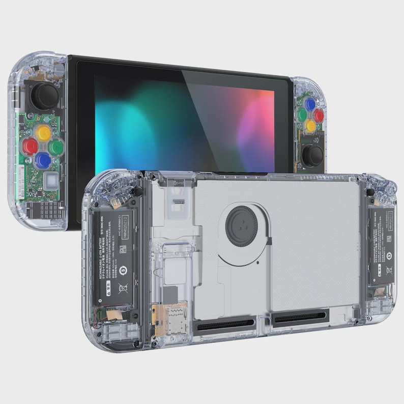 May include: A handheld video game console featuring a transparent clear plastic shell that reveals internal components, including a cooling fan, battery, and circuit boards. The device has colorful action buttons and a black screen display.