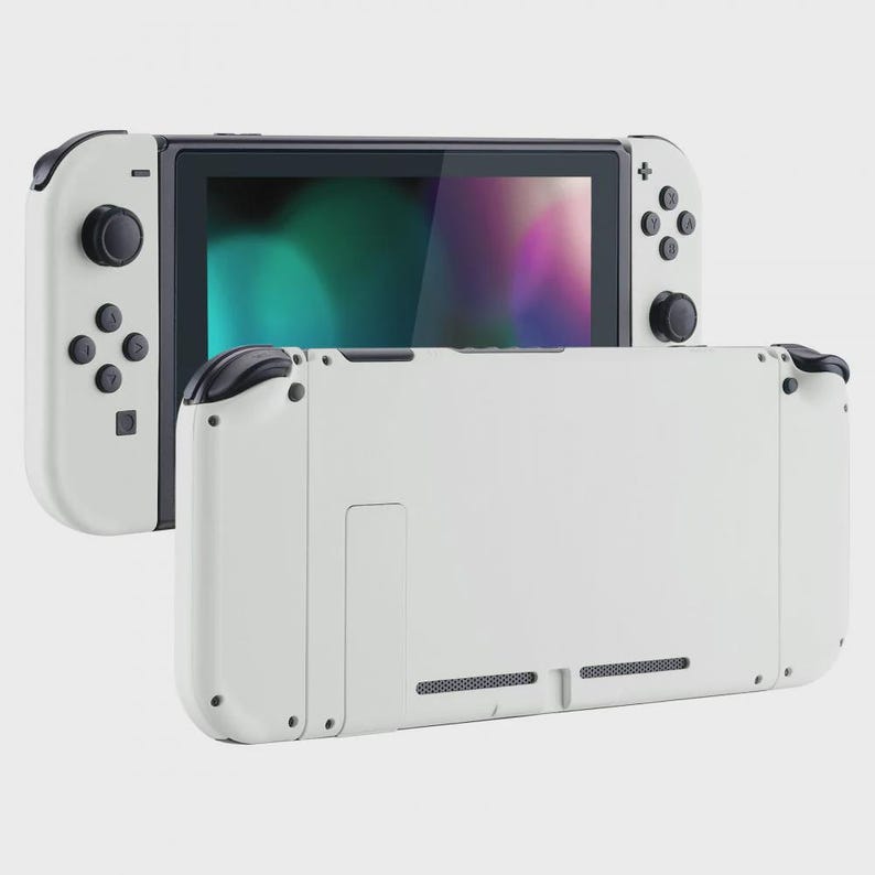May include: A white handheld video game console featuring a central screen with a colorful display and detachable white controllers on each side. The device includes black buttons, joysticks, and a rear panel with visible ventilation grilles.