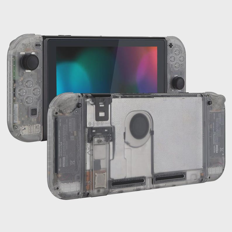 May include: A handheld gaming console featuring a clear, transparent plastic shell that reveals internal components. The device includes two detachable side controllers with black joysticks and buttons, and a central screen displaying a colorful gradient.