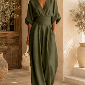 May include: An olive green jumpsuit featuring a deep V-neckline, three-quarter length sleeves with folded cuffs, and a wide, cinched waistband. The garment has wide-leg trousers with side pockets and is branded with the text LUNARO FASHION.