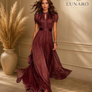 May include: A floor-length burgundy dress with short puff sleeves, a high neckline featuring a keyhole cutout, and a cinched waist. The garment has a sheer, flowing skirt and delicate lace trim along the collar. The text LUNARO FASHION is visible.