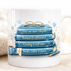 Peut inclure: Mug en céramique blanche avec une pile de livres bleus et des lunettes à monture dorée. Les livres portent les inscriptions "Just one more chapter", "Booked & caffeinated", "Reading is self care" et "Books, coffee & peace". Une petite tasse à café bleue et un stylo sont également représentés.