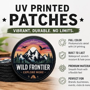 Könnte beinhalten: Ein Stapel runder Aufnäher mit schwarzem Rand, die einen Berg und einen Sonnenuntergang zeigen. Der Text "WILD FRONTIER - EXPLORE MORE" ist zu sehen. Das Bild zeigt auch den Text "UV PRINTED PATCHES" und "VIBRANT. DURABLE. NO LIMITS."