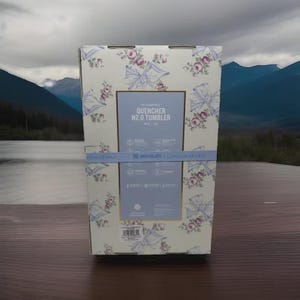 May include: A box for a Stanley Quencher H2.0 Tumbler, featuring a floral pattern with bows and roses in shades of pink and blue on a cream background. The box has a blue band with the brand name and product details.