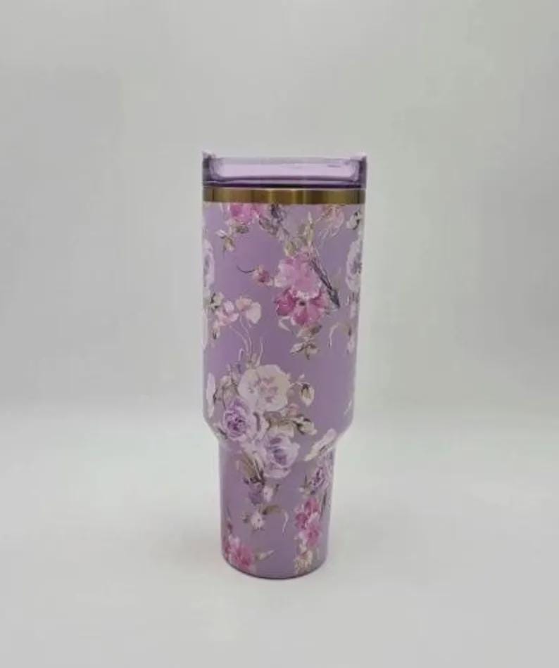 May include: A lilac-coloured tumbler adorned with a floral pattern of pink and white roses. It features a gold band at the top and a clear, rectangular lid. The design is elegant and suitable for everyday use.