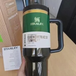 Puede incluir: Un vaso Stanley Quencher H2.0 negro y verde con asa. El vaso tiene una banda verde con el logotipo y el texto de Stanley. El producto est&aacute; dise&ntilde;ado para la hidrataci&oacute;n durante todo el d&iacute;a y tiene 1,18 litros.