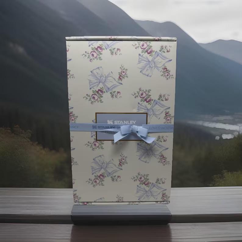 May include: A rectangular gift box with a floral and bow pattern in light blue and pink on a cream background. A light blue ribbon with a bow wraps around the box. The box has the "STANLEY" logo.