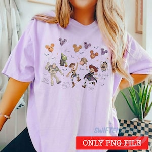 May include: A light purple t-shirt featuring a graphic print of Toy Story characters including Buzz Lightyear, Woody, Jessie, and Mr. Potato Head, each holding a Mickey Mouse-shaped balloon. The text includes character names and small bats.