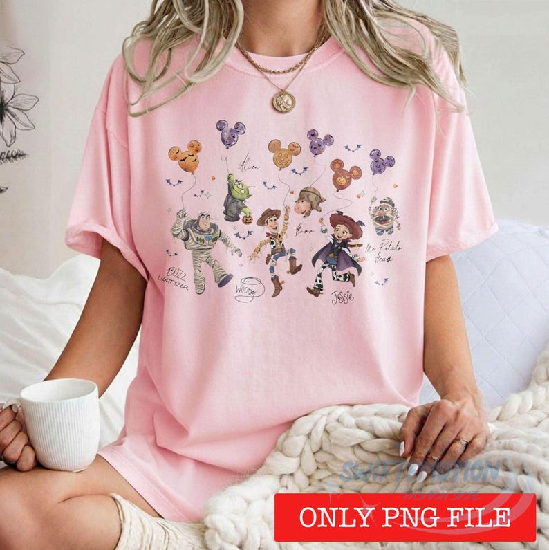 May include: A light pink t-shirt featuring a graphic print of various animated characters including Buzz Lightyear, Woody, and Jessie holding Mickey Mouse-shaped balloons. The design includes handwritten-style text labels for each character.