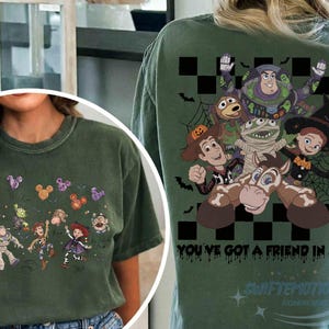 May include: A dark olive green t-shirt featuring Toy Story characters in Halloween costumes. The front shows small character graphics with Mickey-shaped balloons. The back displays a large graphic of the characters with the text You've Got A Friend In Me.