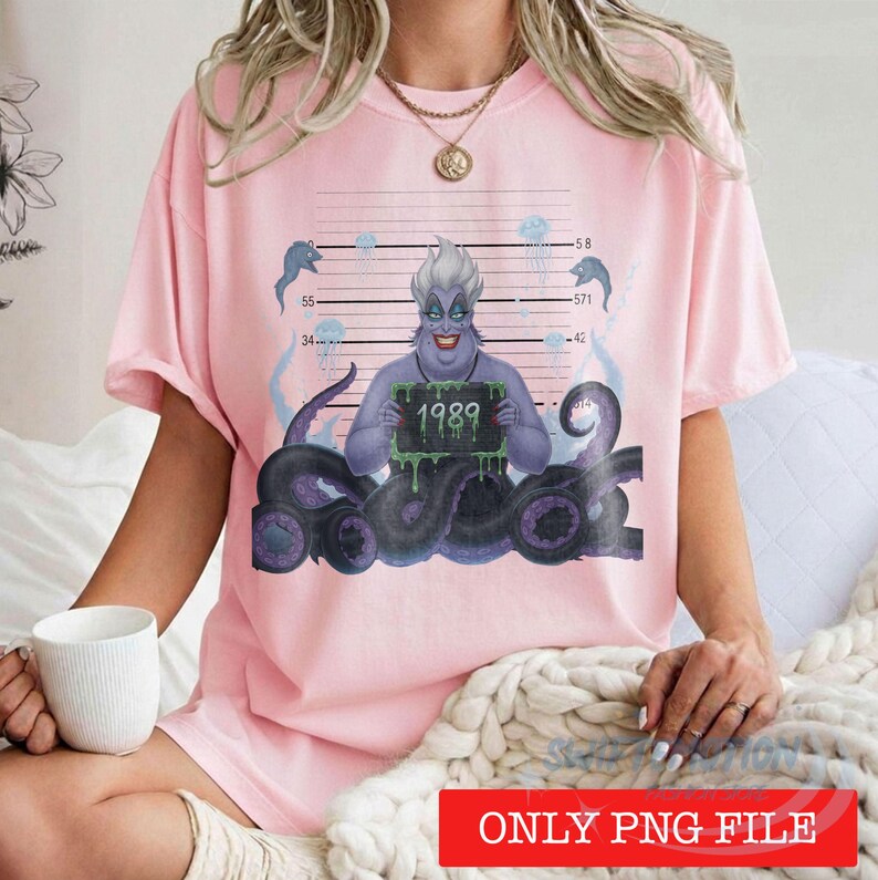 May include: A light pink t-shirt featuring a graphic of a purple sea witch character with tentacles, holding a sign that reads 1989 against a mugshot background with horizontal lines and jellyfish illustrations in blue and white tones.