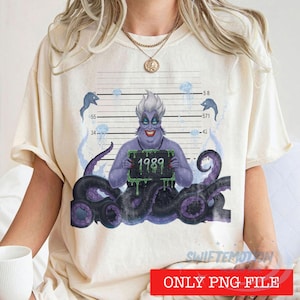 May include: A cream-colored t-shirt featuring a graphic of a purple sea witch with tentacles, positioned against a mugshot height chart background. The character holds a sign with the text 1989, surrounded by small blue jellyfish and fish.