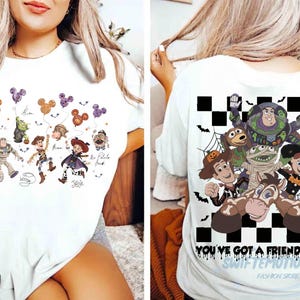 May include: A white t-shirt featuring Toy Story characters in Halloween costumes. The front displays Buzz, Woody, and Jessie with Mickey-shaped balloons. The back shows a checkered pattern with the characters and the text You've Got A Friend In Me.
