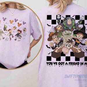 May include: A light purple t-shirt featuring a large graphic on the back of Toy Story characters in Halloween costumes against a black and white checkered background with the text "YOU'VE GOT A FRIEND IN ME" and a smaller front chest graphic.