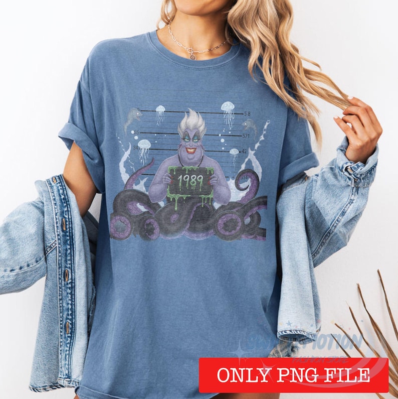 May include: A blue t-shirt featuring a graphic print of a purple-skinned character with white hair holding a sign that reads 1989. The design includes dark purple tentacles, jellyfish illustrations, and a police mugshot height chart background.