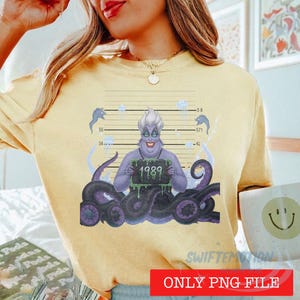 May include: A pale yellow t-shirt featuring a graphic of a purple sea witch with tentacles holding a mugshot sign that reads 1989. The design includes a height chart background with numbers and small jellyfish illustrations in blue and white.