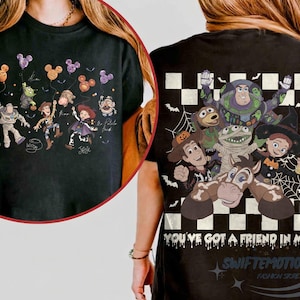 May include: A black t-shirt featuring Toy Story characters in Halloween costumes. The front shows characters with Mickey-shaped balloons. The back displays characters over a checkered pattern with the text "YOU'VE GOT A FRIEND IN ME" in a dripping font.