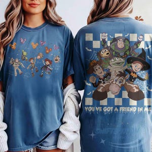 May include: A blue t-shirt featuring Toy Story characters. The front displays small illustrations of characters with Mickey-shaped balloons. The back shows a large graphic of Buzz Lightyear, Woody, Jessie, and Bullseye with the text YOU'VE GOT A FRIEND IN ME.