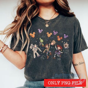 May include: A charcoal gray t-shirt featuring a graphic print of Toy Story characters including Buzz Lightyear, Woody, and Jessie. The design includes Mickey-shaped balloons, stars, and character names written in a cursive script font.