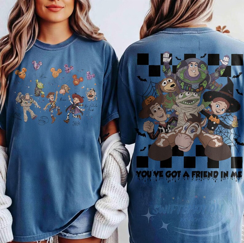 May include: A blue t-shirt featuring Toy Story characters in Halloween costumes. The front shows small character illustrations with Mickey-shaped balloons. The back displays a large graphic of Buzz Lightyear, Woody, and friends with a black and white checkerboard pattern, spiderwebs, and the text "YOU'VE GOT A FRIEND IN ME."