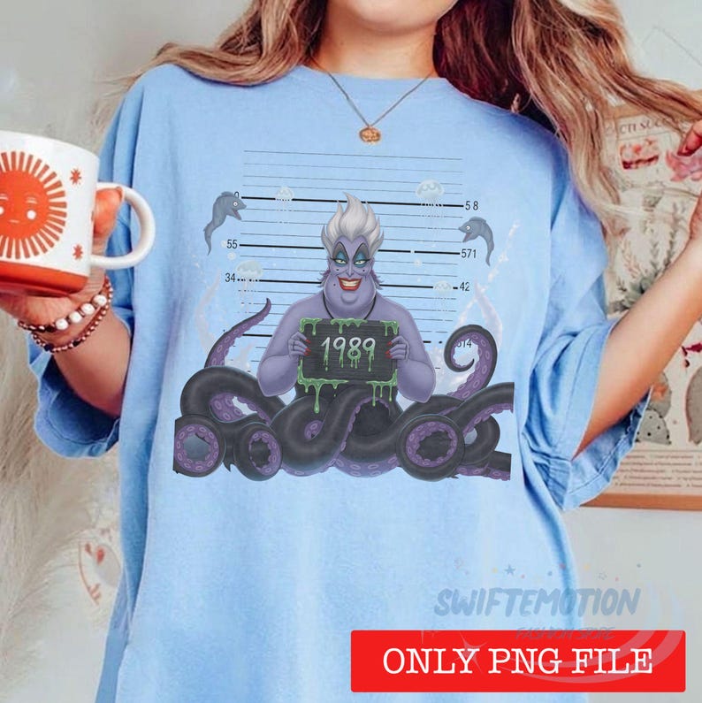 May include: A light blue t-shirt featuring a graphic of a purple sea witch with tentacles holding a sign that reads 1989 against a mugshot background with height markers. The design includes small fish illustrations and a dark purple tentacle base.