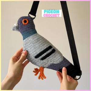 May include: A handmade crochet pigeon-shaped bag in grey, blue, and black, with orange detailing. It has a black strap and the text "PIGEON CROCHET". The bag is designed to look like a pigeon, with detailed crochet work.