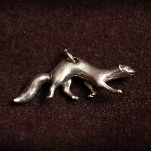 May include: A silver charm in the shape of a weasel or ferret. The charm is detailed and has a realistic appearance.