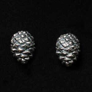 May include: A pair of silver earrings shaped like pine cones.