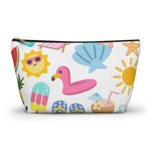 Puede incluir: Un estuche blanco con cremallera que presenta un colorido patrón de temática veraniega con un flotador de flamenco rosa, soles amarillos con gafas de sol, conchas azules, estrellas de mar naranjas, sandía, piña, un helado y un coco.