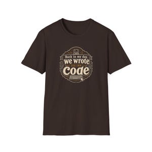Peut inclure: T-shirt marron foncé avec un motif rétro. Le motif comprend le texte "Back in my day, we wrote our own code" avec une illustration d'ordinateur et de clavier vintage. Le design utilise des couleurs marron et crème.