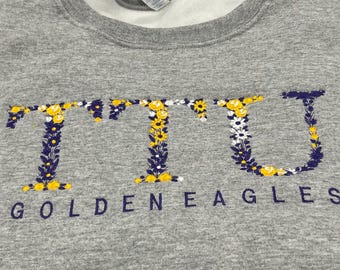May include: Gray sweatshirt with a floral design spelling out "TTU" and the text "Golden Eagles" underneath.